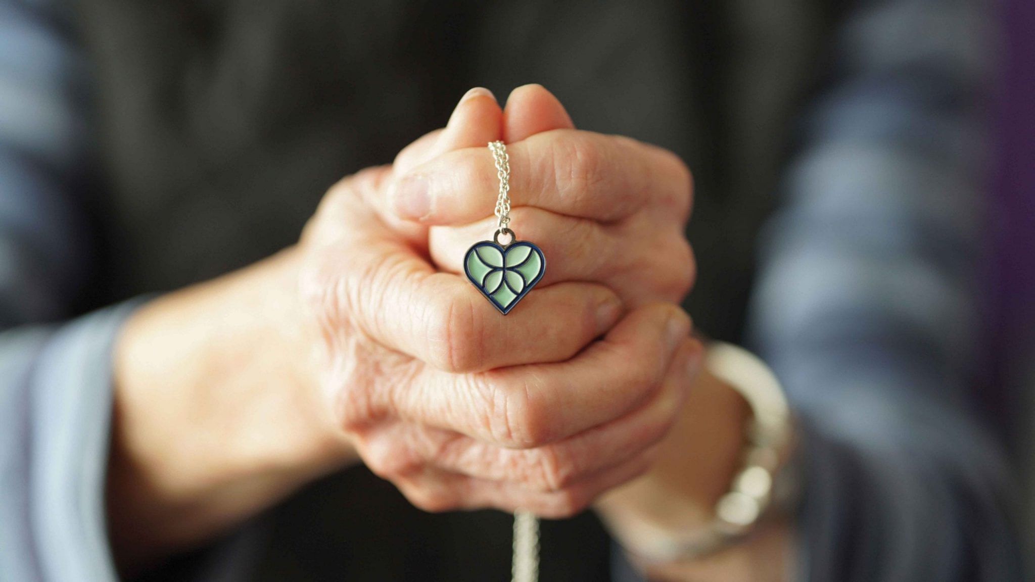Senior woman holding onto a necklace with a charm of the EverHeart Hospice butterfly heart